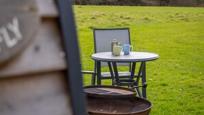 A table with a pitcher and mug, a chair, and a wheelbarrow in a grassy outdoor area. - Dragonfly - sleeps 2 guests  in 1 bedroom (Norwich)