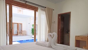 Ein Hotelzimmer mit Bett, einem Holztisch und Blick auf einen Swimmingpool und eine Sitzgelegenheit im Freien.