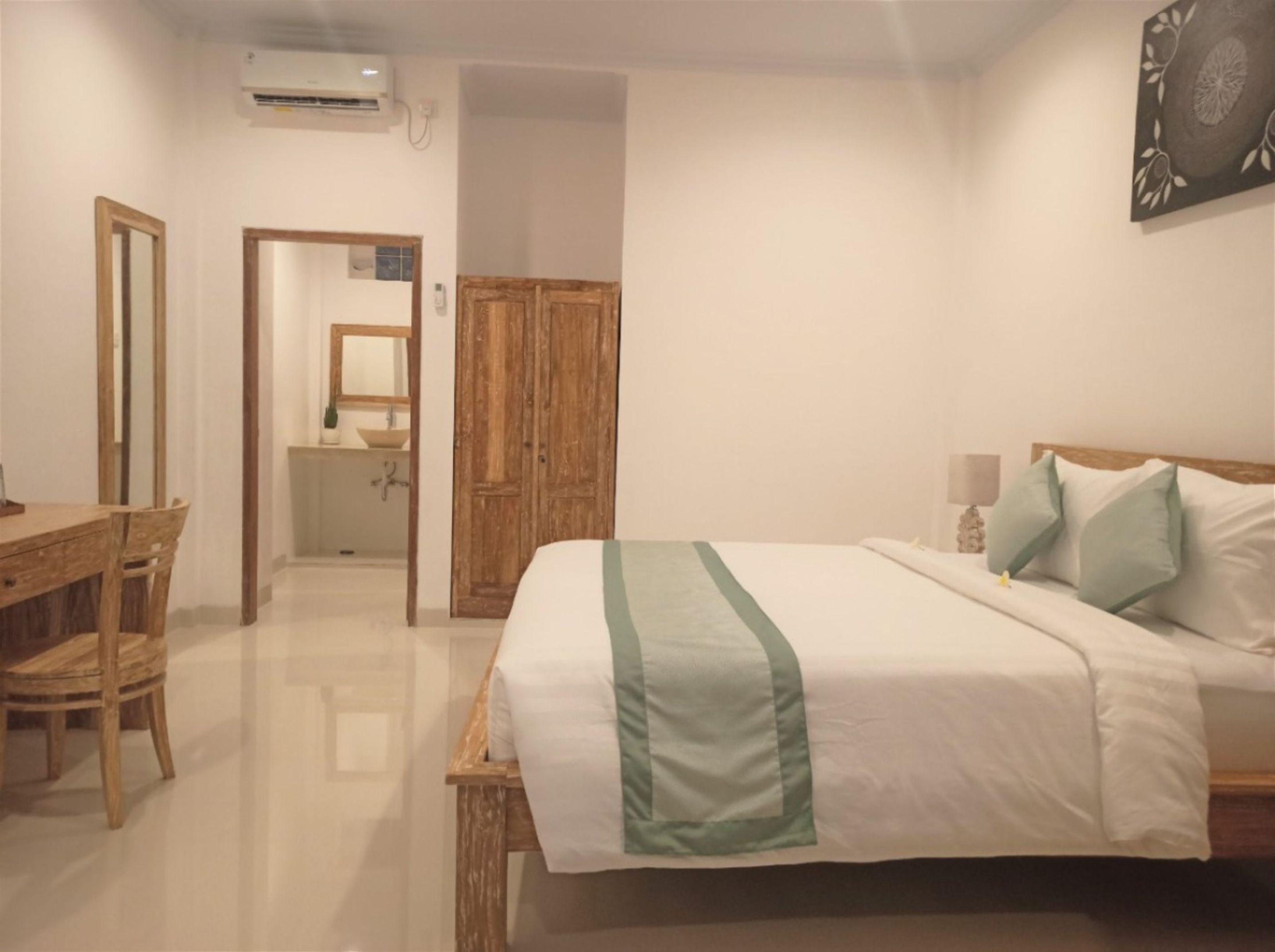 Un dormitorio con una cama, un escritorio de madera, un espejo y un guardarropa.