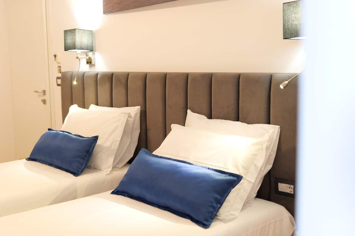 A hotel room with two beds, each with white and blue pillows, and a brown headboard.
