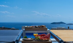 Una bandeja de comida y bebidas sobre una mesa junto a la piscina, con vista al mar y a las islas.