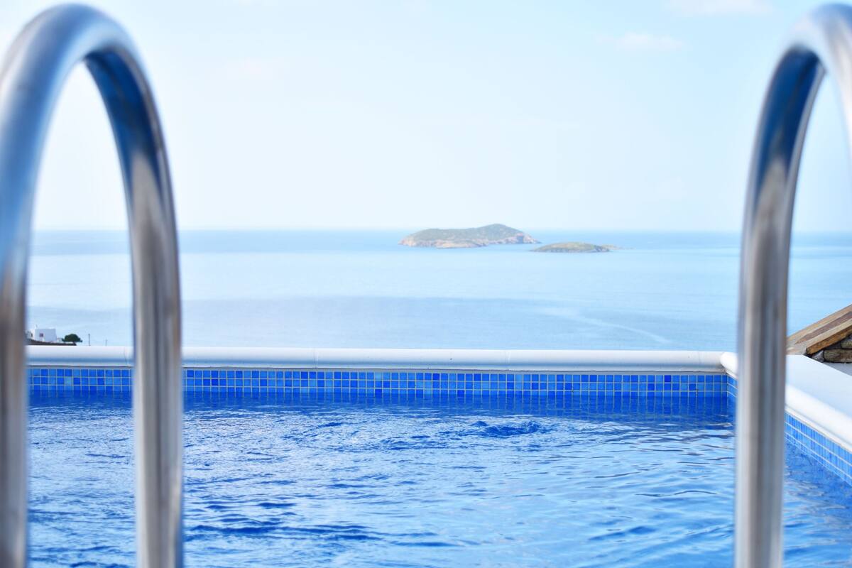 A swimming pool with clear blue water, a view of the sea, and a distant island.