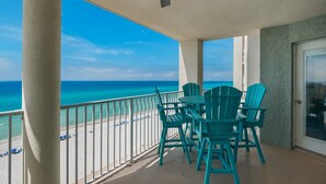 A balcony with a view of the beach and ocean, featuring a table and four chairs.