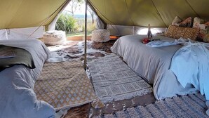A tent with two beds, a central pole, and a view of the outdoors.