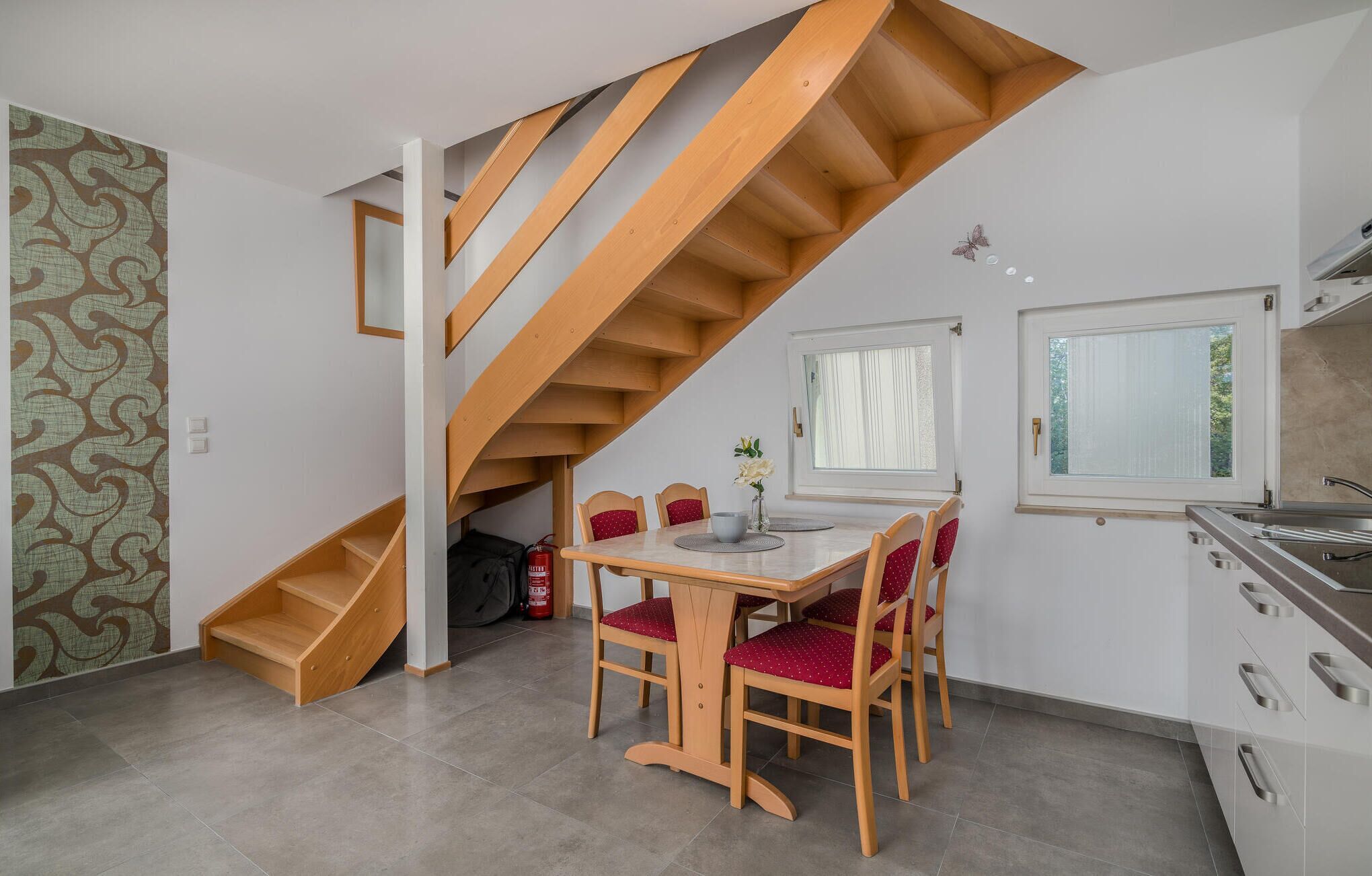 Een kleine keuken met een houten trap, een eethoek met rode stoelen, en een raam met uitzicht.