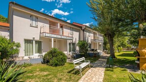 A row of two-story buildings with balconies, a stone pathway, and outdoor seating. - 1 bedroom beach front apartment in Baska (Baska)
