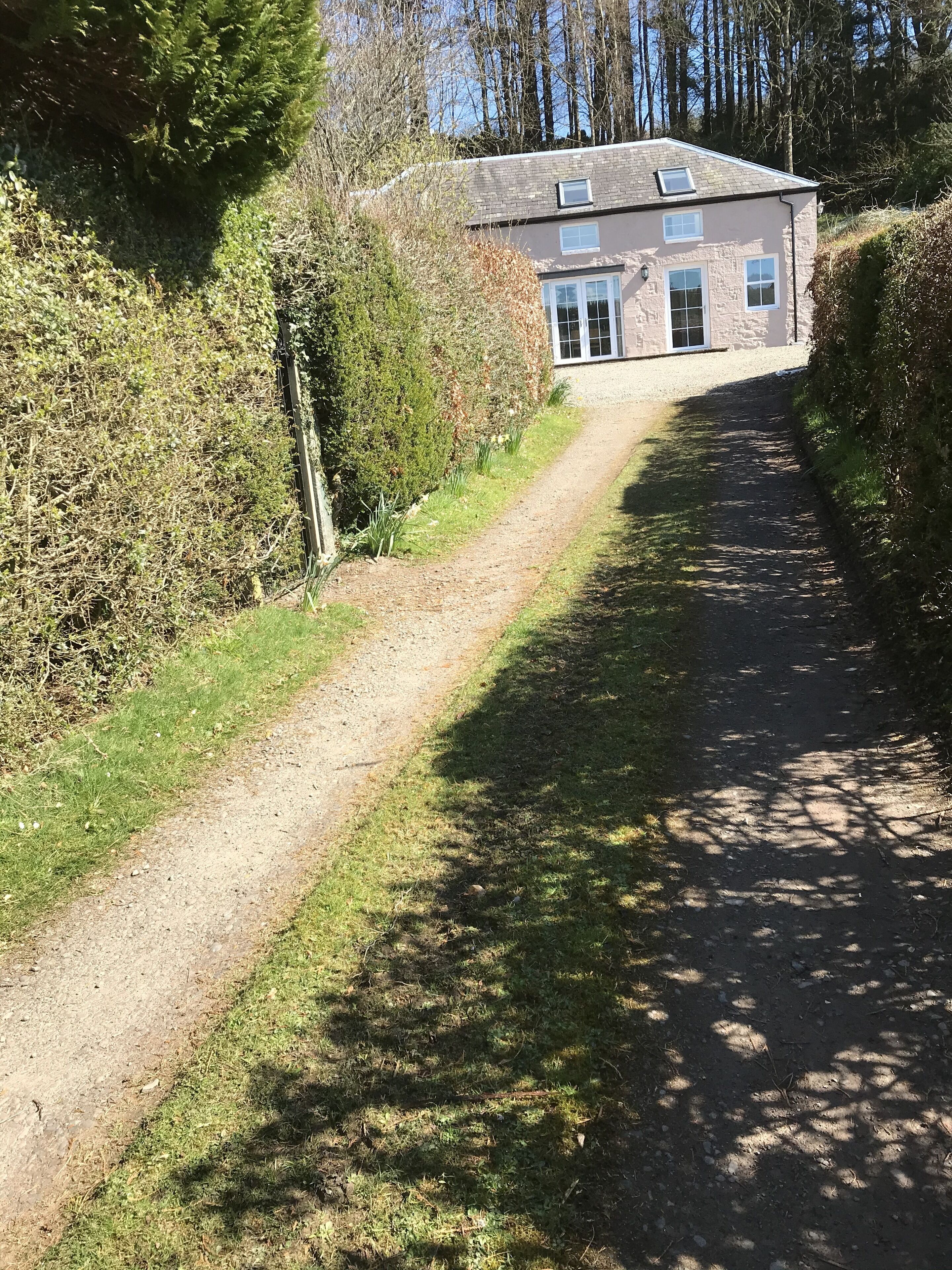Ein Kiesweg führt zu einem Steinhaus mit geneigtem Dach und mehreren Fenstern.