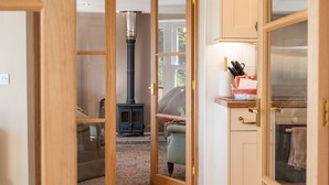 A cozy room with a wooden door, a fireplace, a sofa, and a kitchen area with a stove and utensils. - Luxury Cottage in the Scenic Borders of Scotland (Canonbie)