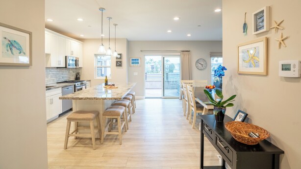 Une cuisine moderne dotée d’un îlot central, de tabourets de bar en bois et d’un coin repas avec une table et des chaises.