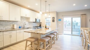 Une cuisine moderne avec des meubles blancs, un plan de travail en granit, un îlot central doté de tabourets et une vue sur un balcon.