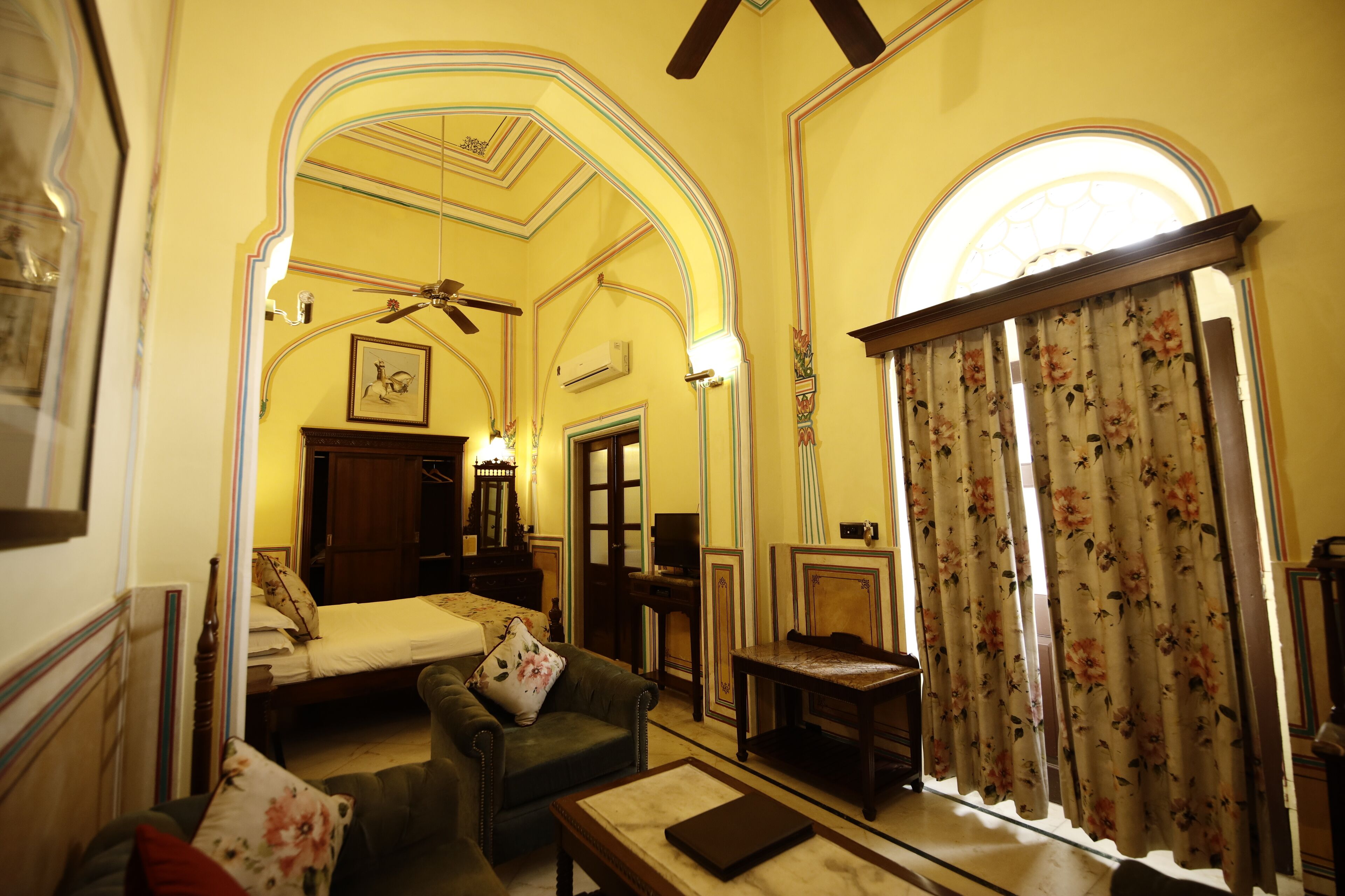 Una habitación con cama, sofá, mesa y ventana con cortinas florales.