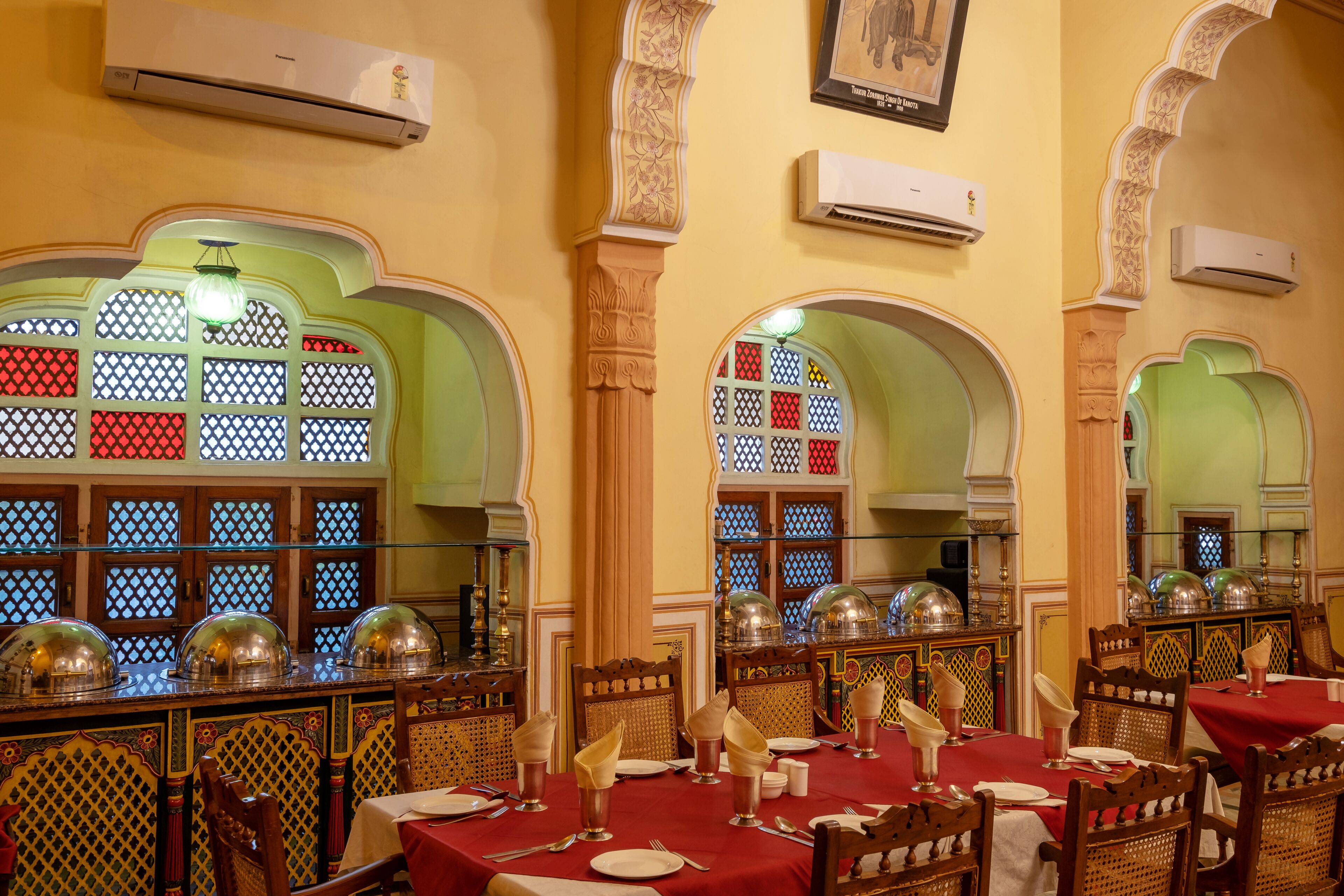 Un restaurante con decoración tradicional, con ventanas arqueadas de vidrio emplomado, muebles de madera ornamentados y un mantel rojo.