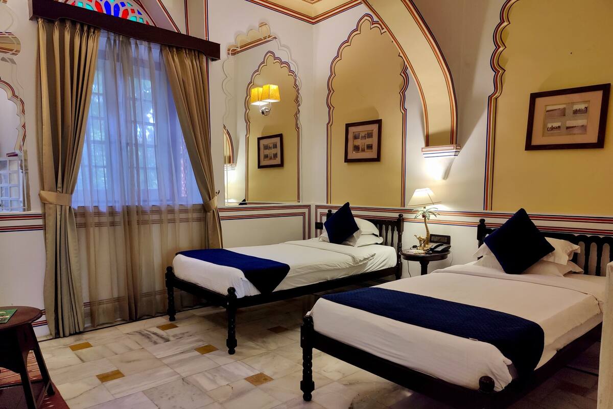 Une chambre d’hôtel avec deux lits, une table de chevet, une lampe et une fenêtre avec des rideaux.