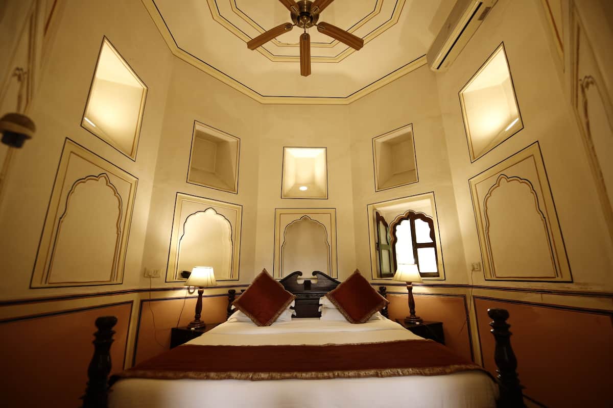 Une chambre d’hôtel avec un grand lit, un ventilateur de plafond et plusieurs lampes fixées au mur.