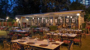 Een terras met tafels en stoelen, een overdekt zitgedeelte met ingelijste foto's, en een gebouw op de achtergrond.