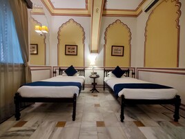 Quarto de hotel com duas camas, uma mesa pequena e uma luminária.