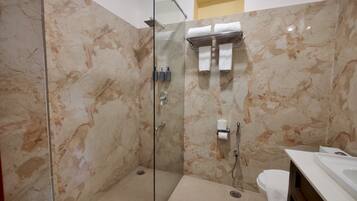 A modern bathroom with a glass-enclosed shower, marble walls, a toilet, and a sink.