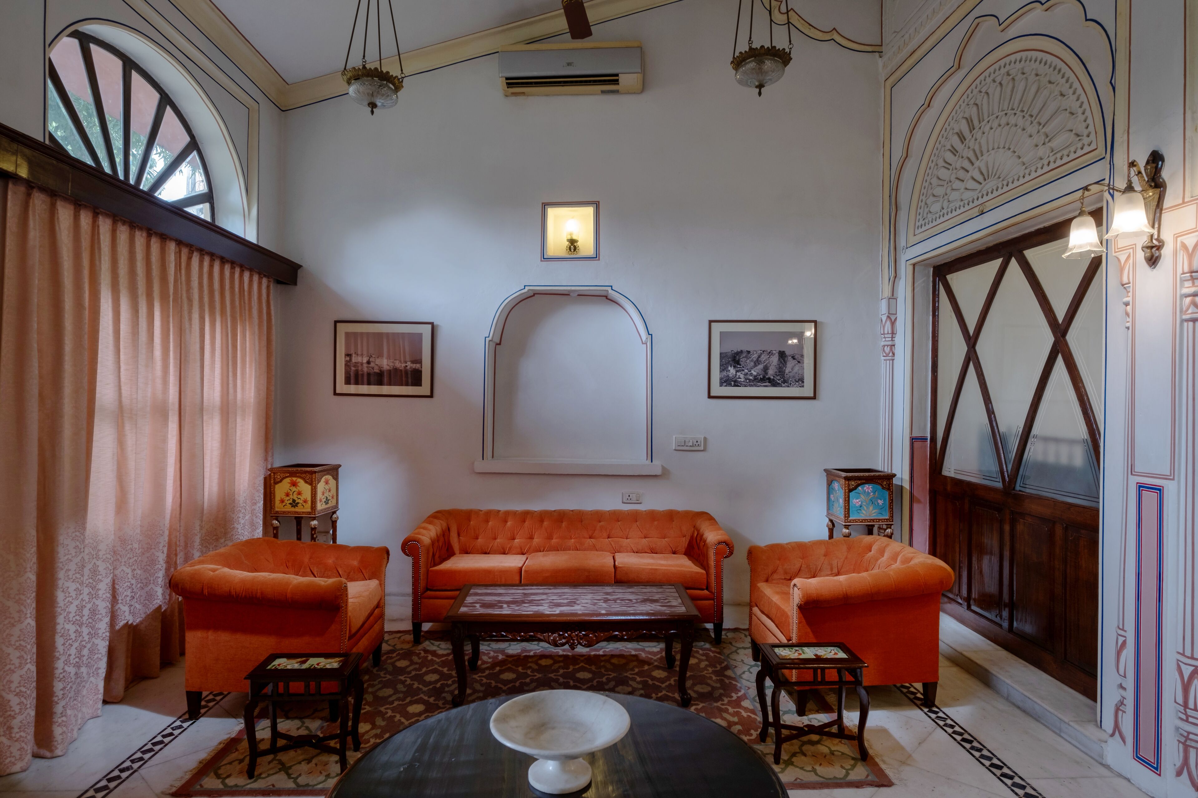 A room with a large arched window, a sofa set, a table, and a decorative mirror.