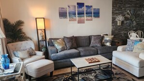 Una sala de estar con un sofá gris, sillones blancos, una mesa de centro y una pared decorada con motivos marinos.