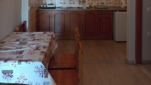 A compact kitchen with an arched doorway, wooden cabinets, a small refrigerator, and a dining area with a table and chairs. - Dionisos Apartments (Corfu)