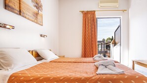 A hotel room with two beds, a balcony, and a view of the cityscape. - Dionisos Apartments (Corfu)