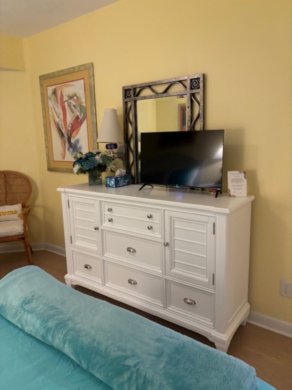 Un dormitorio con un aparador blanco, un televisor de pantalla plana, una lámpara y un cuadro en la pared.