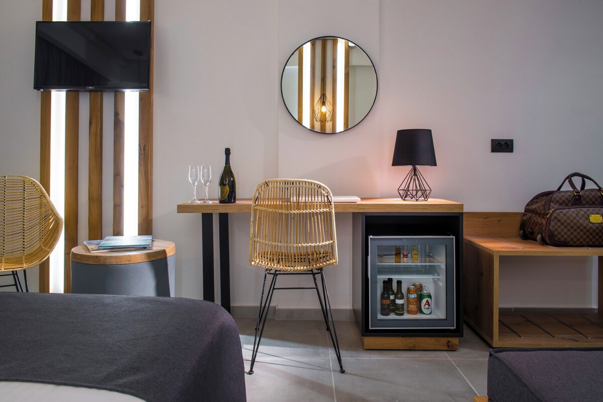 Una habitación de hotel moderna con una cama, un escritorio con silla, televisión, espejo, lámpara y minibar.