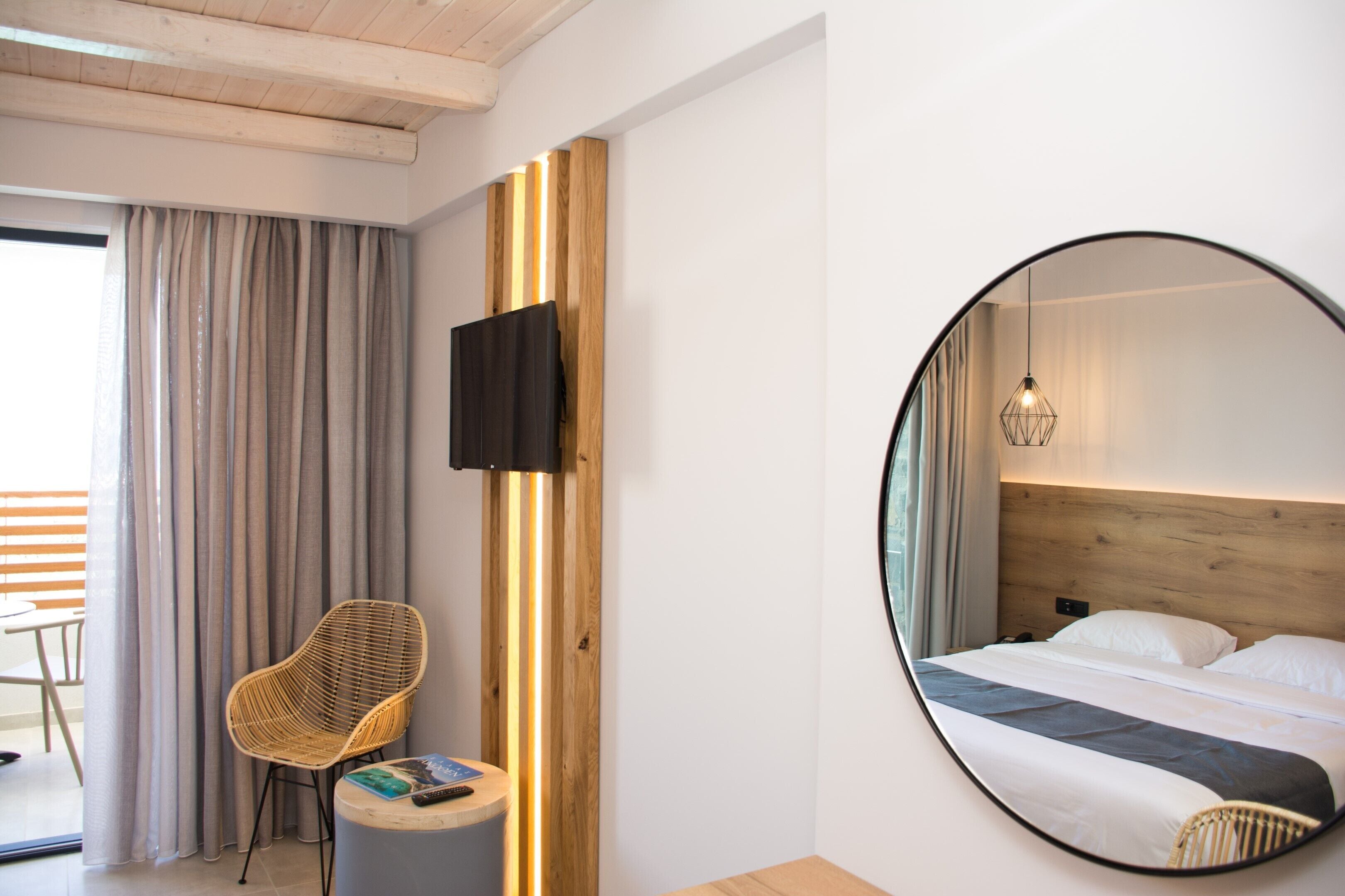 Ett hotellrum med en säng, en rund spegel, en stol, ett litet bord och en tv på väggen.