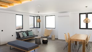 Un espacio habitable moderno con un sofá, una mesa de comedor con sillas, una lámpara colgante y ventanas amplias.