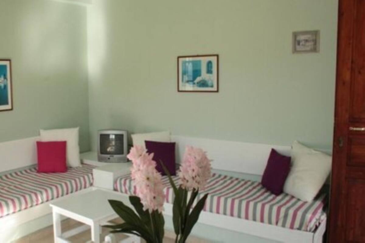 Ein Wohnzimmer mit zwei weißen Sofas, gestreifte Kissen, einem kleinen weißen Tisch und einem Fernseher.