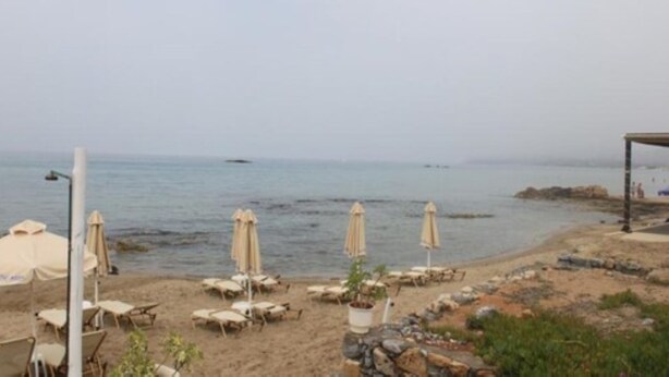Une plage avec des chaises longues et des parasols, un rivage rocheux et une vue sur la mer.