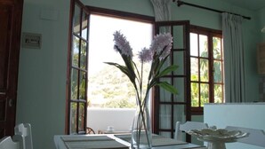 Un espace repas comprenant une table, des chaises, un vase avec des fleurs et une vue sur la verdure à l’extérieur.