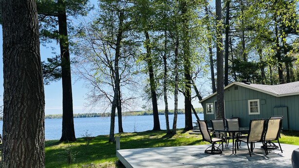 Terraza junto al lago con mobiliario exterior y una cabaña pequeña.