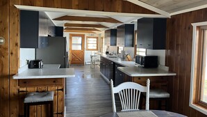 Una cocina moderna con detalles de madera, una isla central y un comedor con una silla blanca.