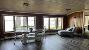 Un espacio amplio con una mesa de comedor y sillas, un sofá, ventanas grandes con vista a una masa de agua y paneles de madera en las paredes.