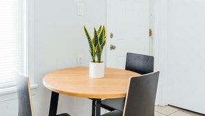 A round wooden table with a potted plant, two black chairs, and a white door in a room with white walls. - 2R- ❤️ Stylish and Cozy 2BR in Logan Square! (Chicago)