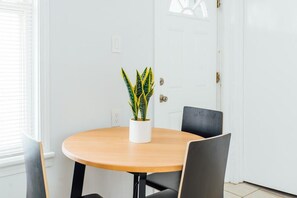 Une table ronde en bois, sur laquelle est posée une plante en pot, deux chaises noires et une porte blanche, dans une pièce aux murs blancs.