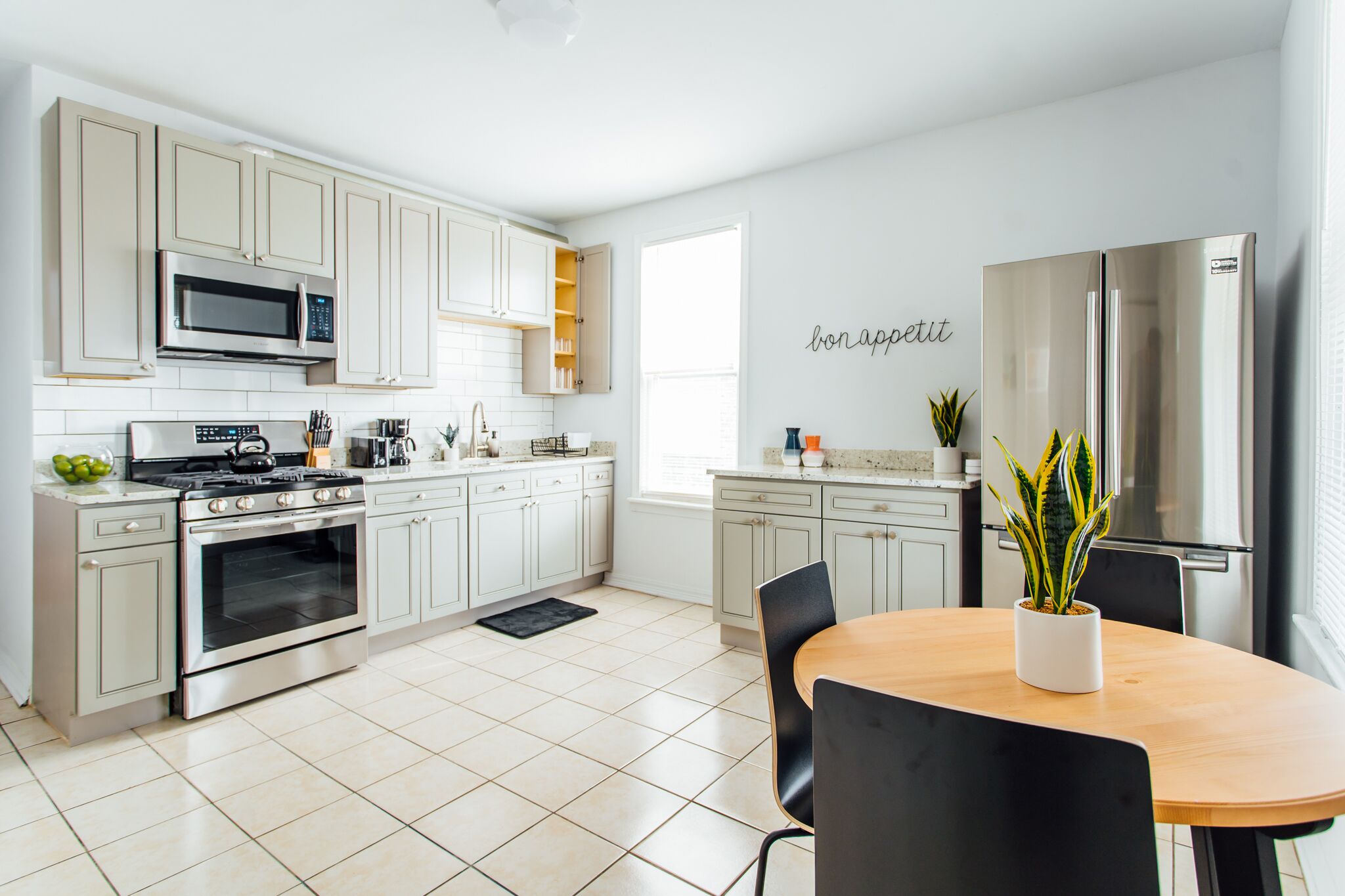 Une cuisine moderne avec des meubles blancs, des appareils en acier inoxydable et un coin repas comprenant une table et des chaises en bois.