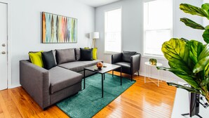 A modern living room with a grey sectional sofa, a black leather chair, a small white table, and a green rug. - 2R- ❤️ Stylish and Cozy 2BR in Logan Square! (Chicago)
