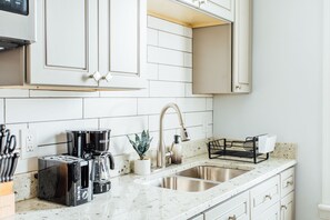 Une cuisine avec des armoires blanches, un évier en acier inoxydable, une machine à café et un grille-pain.