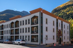 Hotel a più piani con facciata bianca e dettagli verdi, con balconi e uno sfondo montuoso.