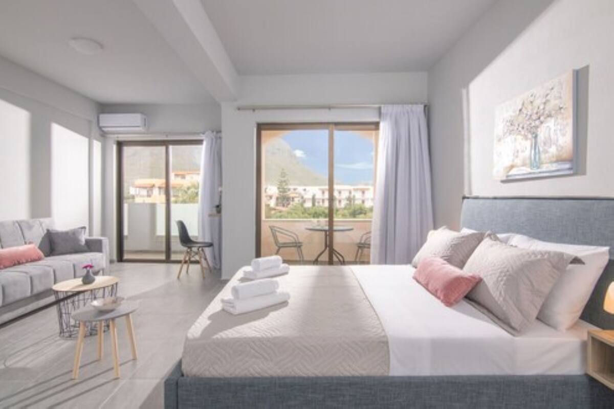 Habitación de hotel moderna con una cama grande, un balcón con mesa y sillas, y vistas de los edificios circundantes.