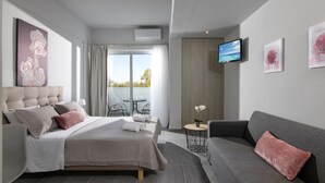 Quarto de hotel moderno com cama, sofá, televisão e varanda com vista.