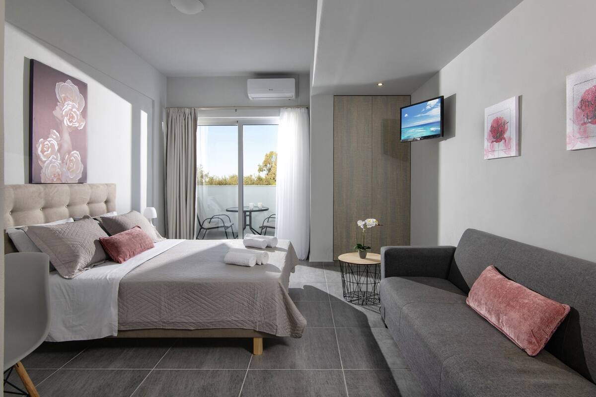 Habitación de hotel moderna con cama, sofá, televisor y balcón con vistas.