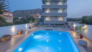 Um edifício moderno com piscina no terraço, rodeado por plantas em vasos e mobiliário de exterior.