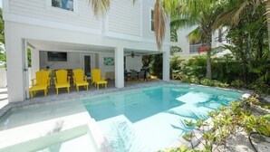 A white two-story house with a swimming pool, yellow chairs, and lush greenery. - Sunset Surf 2201 Ave C 6 Bedroom Home by RedAwning (Bradenton Beach)
