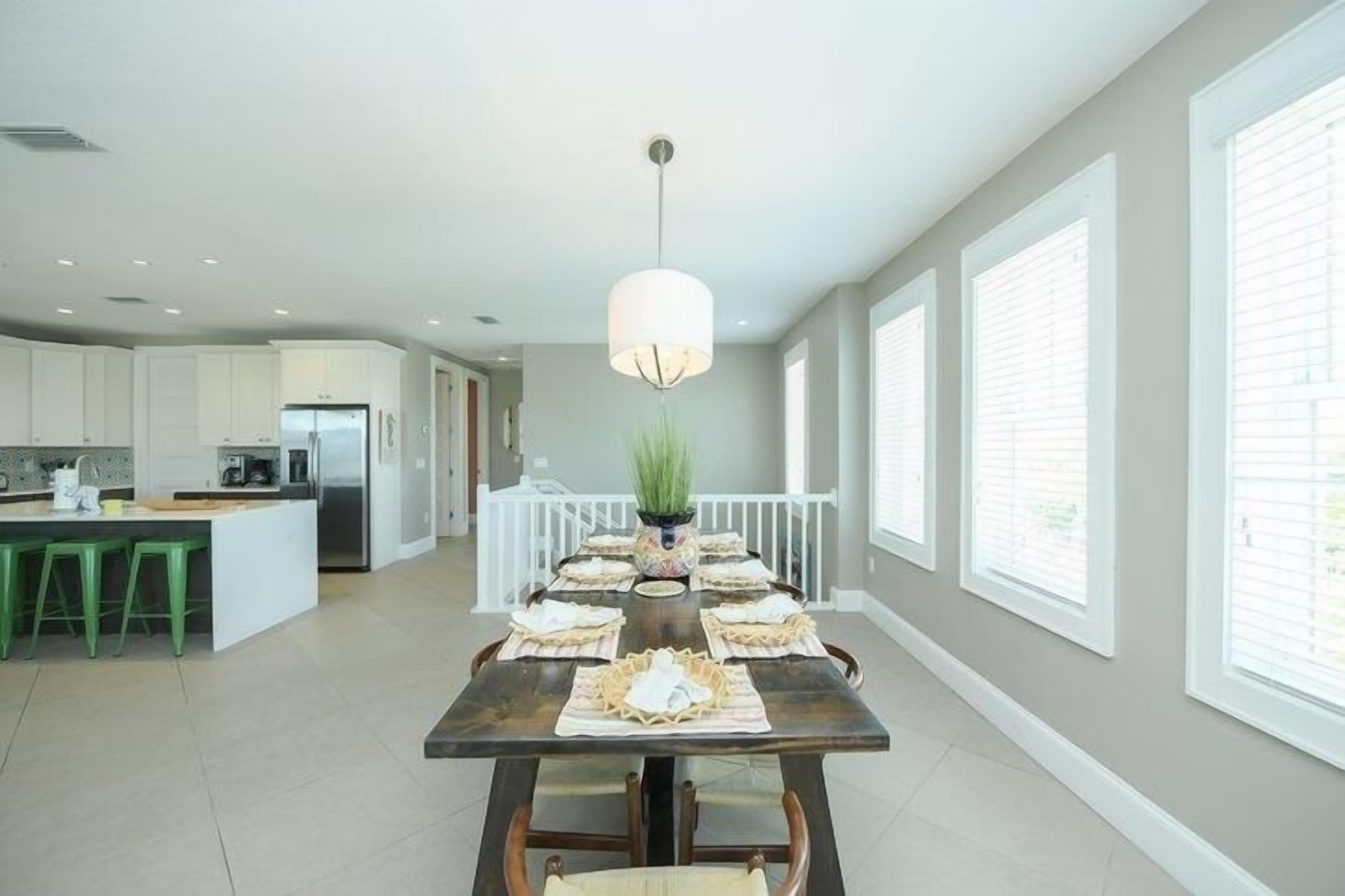 A modern kitchen with white cabinets, a central island with stools, and a dining area with a table set for six.