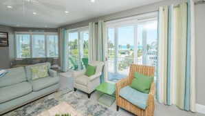 A spacious living room with a large window, a ceiling fan, and a view of the ocean. - Sunset Surf 2201 Ave C 6 Bedroom Home by RedAwning (Bradenton Beach)