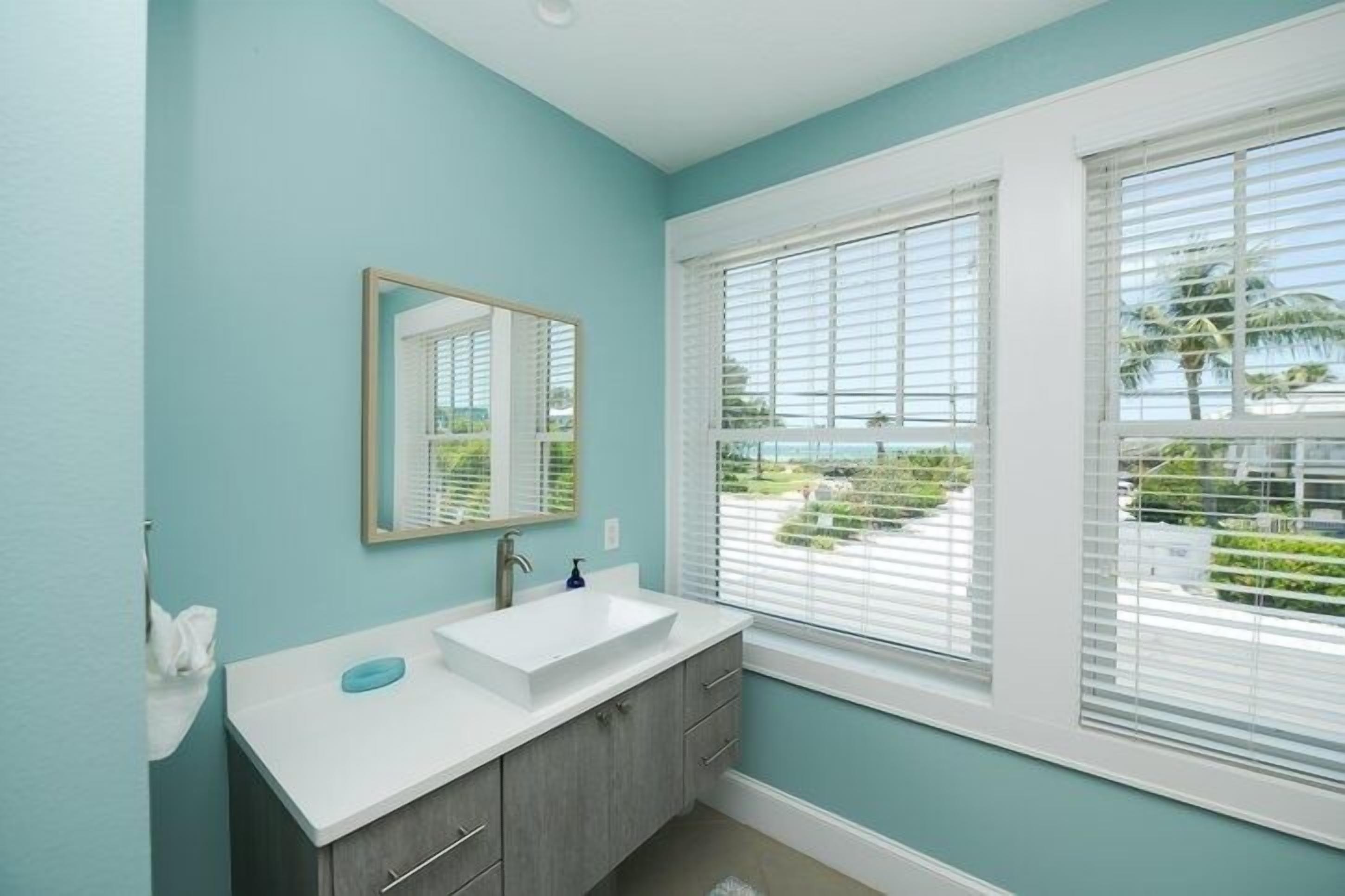 Une salle de bain avec une grande fenêtre, un lavabo blanc et un miroir.
