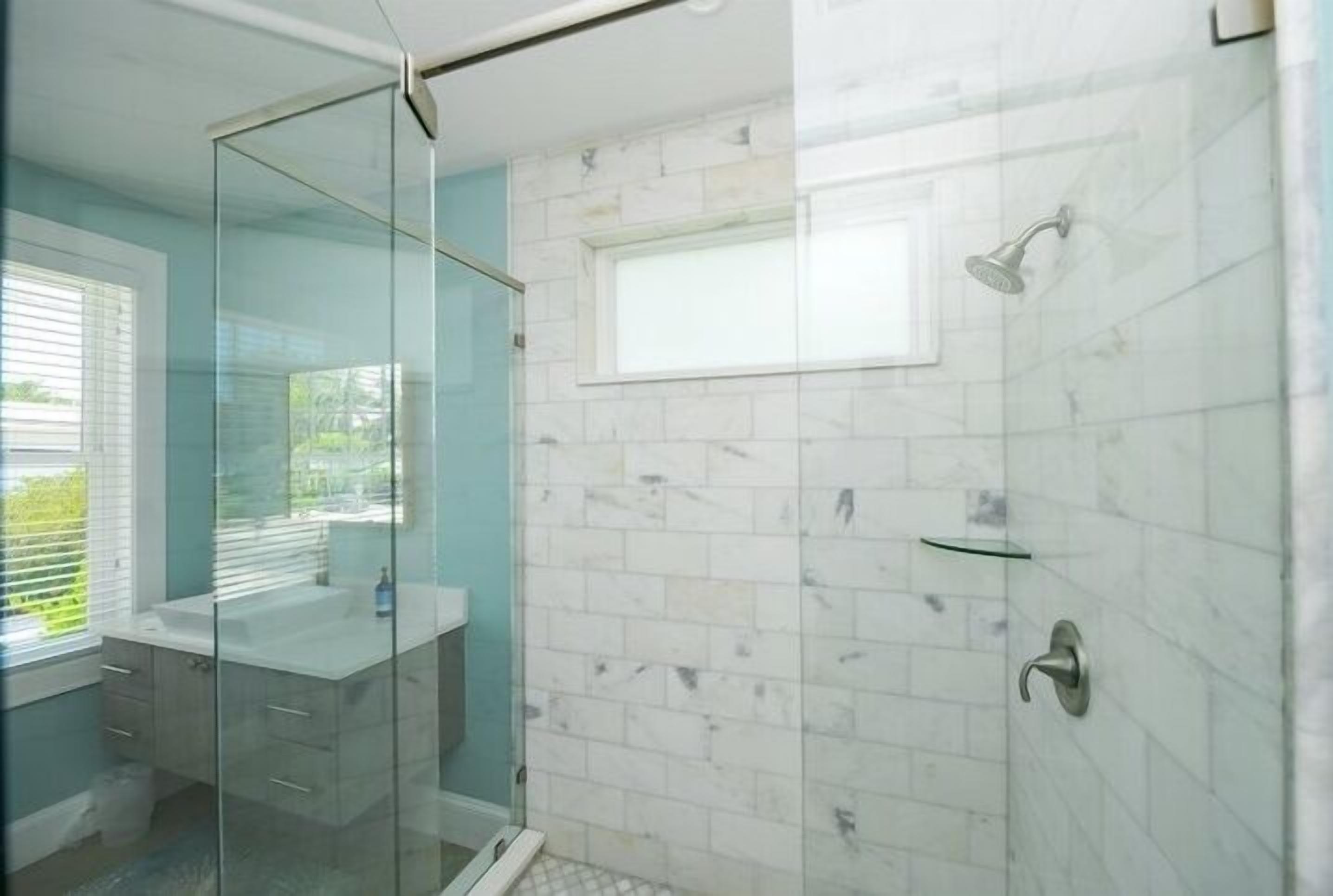 Une salle de bain moderne dotée d’une cabine de douche en verre, d’un espace de douche carrelé de carreaux blancs et d’une paroi en verre qui sépare la douche du reste de la salle de bain.